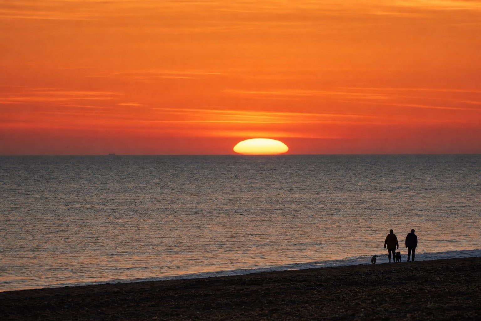 A flattened oval sun setting over the ocean