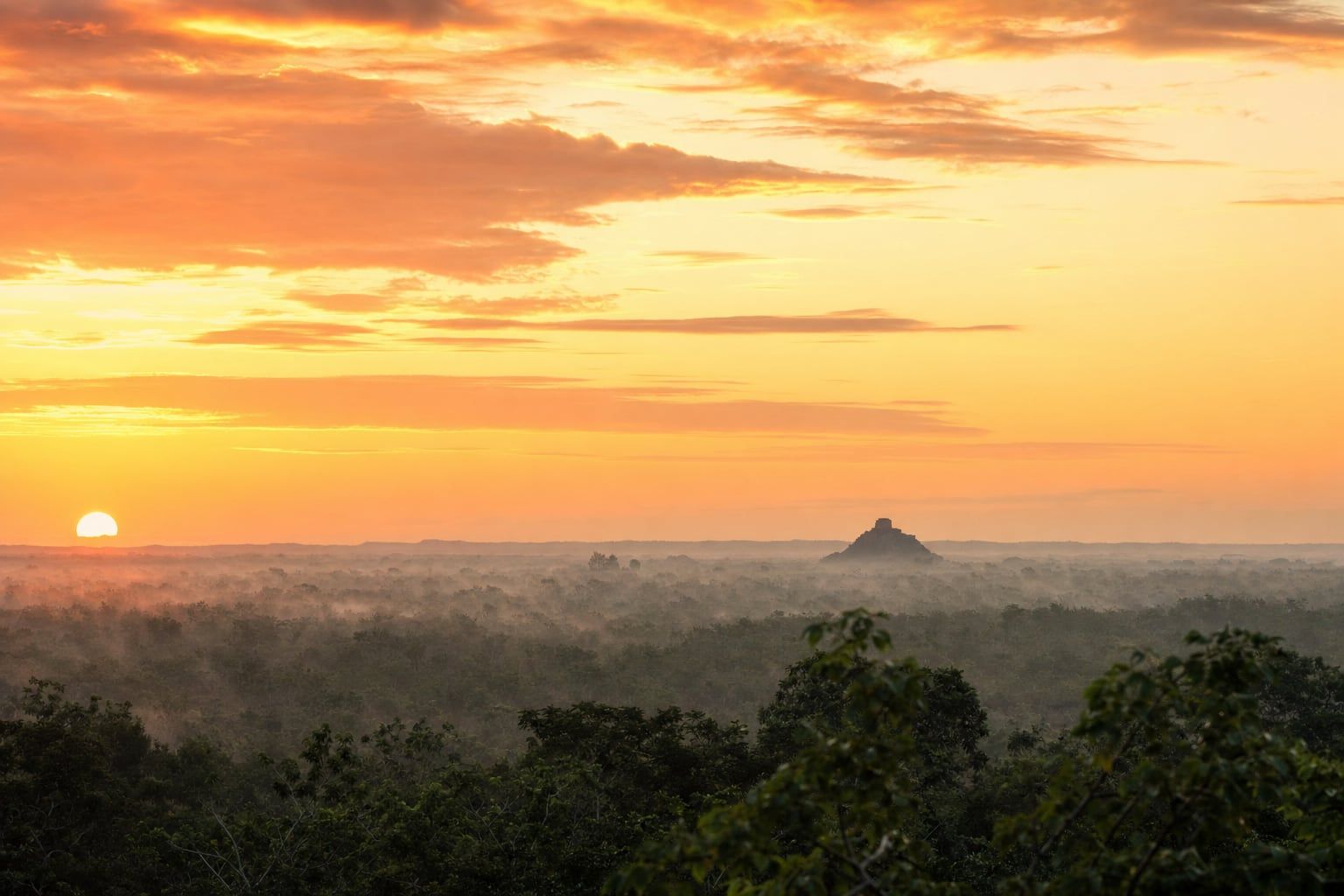 Sunrise over Chichén Itzá Sunrise over the Yucatán jungle with the pyramid of Chichén Itzá far away