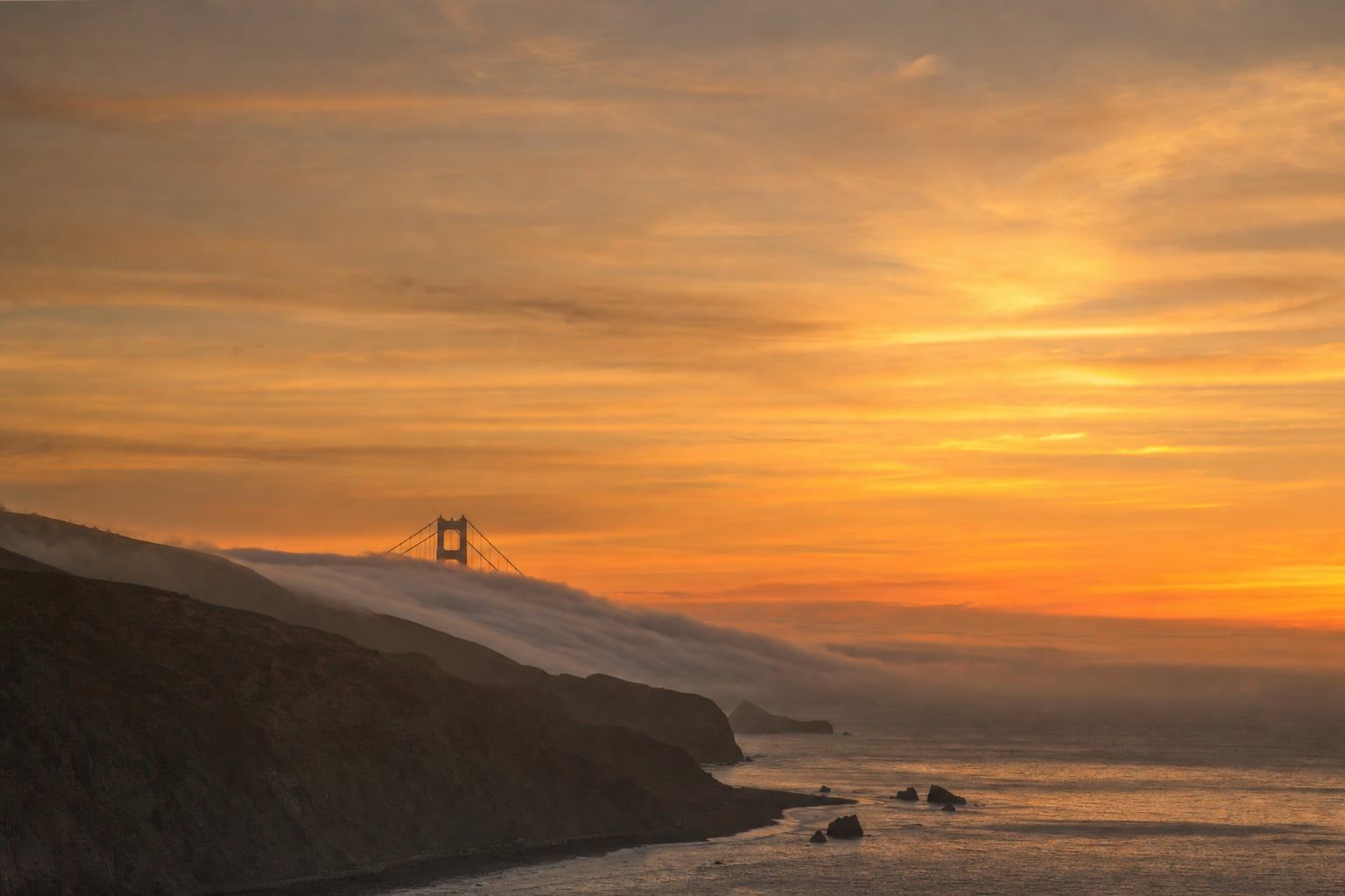 Sunset over the Golden Gate Sunset with fog and the towers of the Golden Gate Bridge far away
