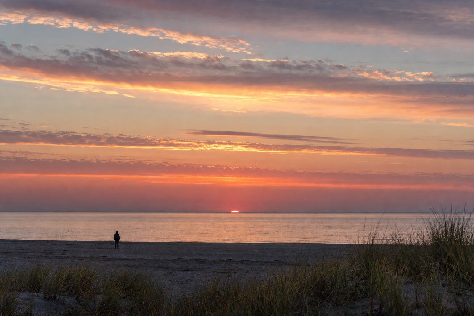 The upper edge of the sun appearing over a calm sea horizon at sunrise
