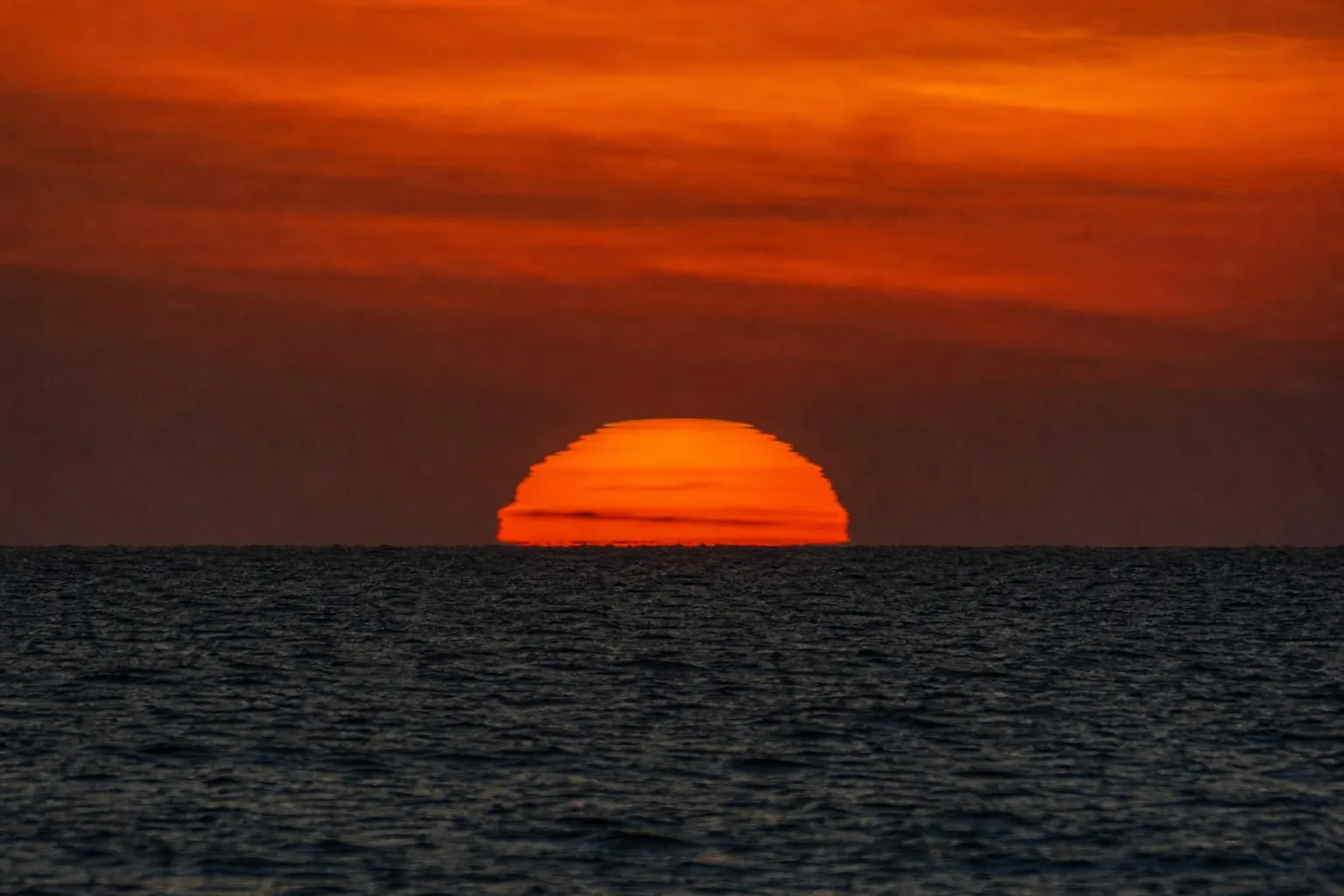 Telephoto view of the sun touching the sea at sunset